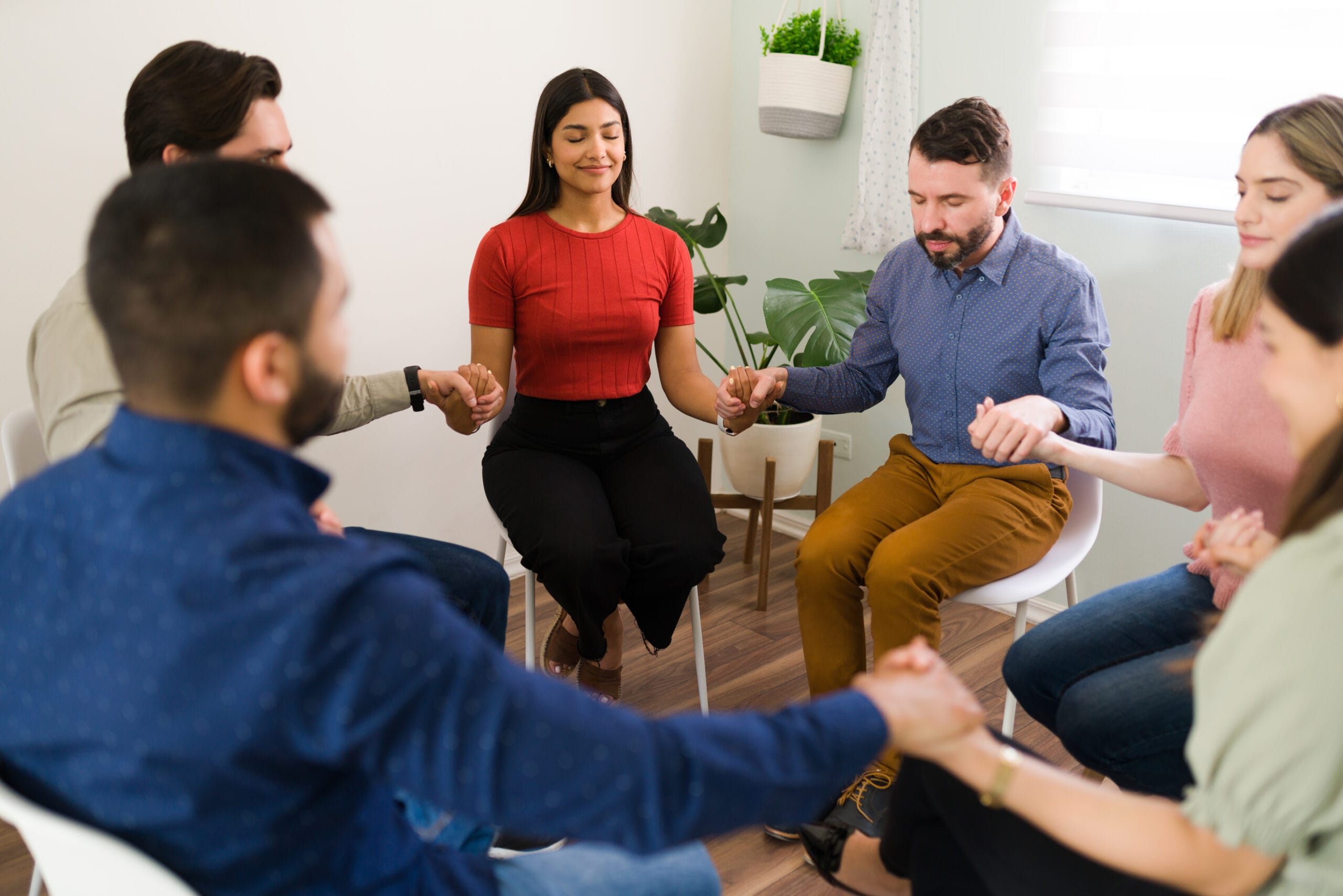 A diverse support group joining hands during a recovery meeting